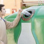 Un joven deposita un envase de vidrio en un contenedor verde en la Comunitat Valenciana